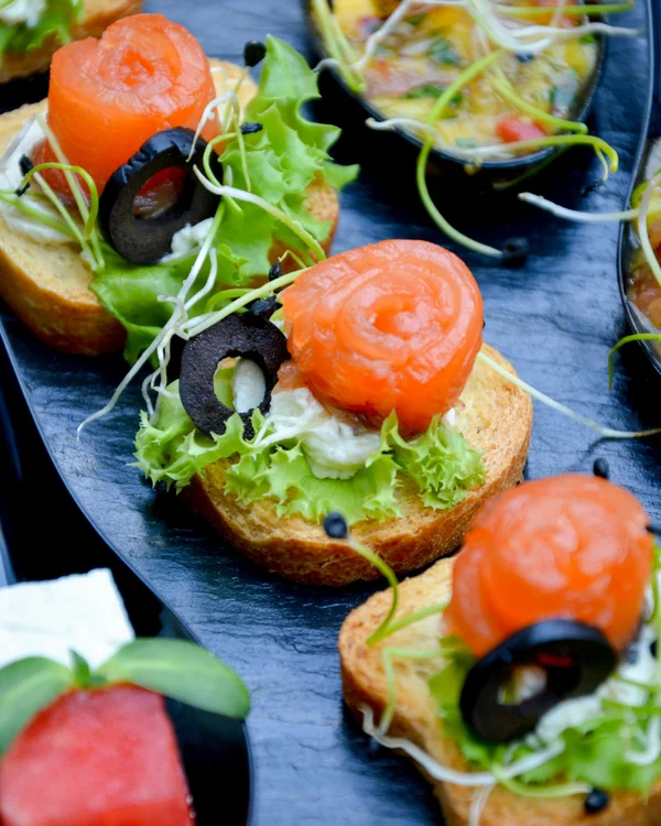 What’s a party without great food and the perfect drink? Plate of canapés with salmon, lettuce, and olives on baguette slices