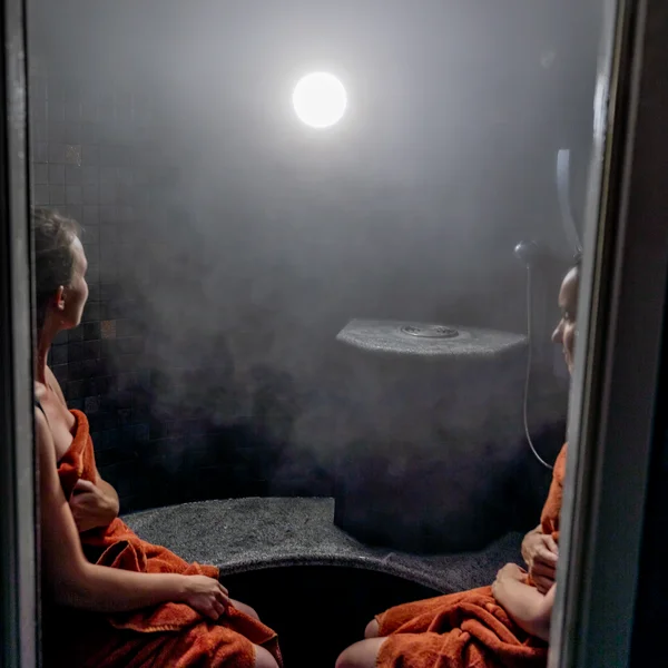 Wellness im Kloster in Deutschland Zwei Frauen in Handtüchern sitzen in einem nebligen Dampfbad