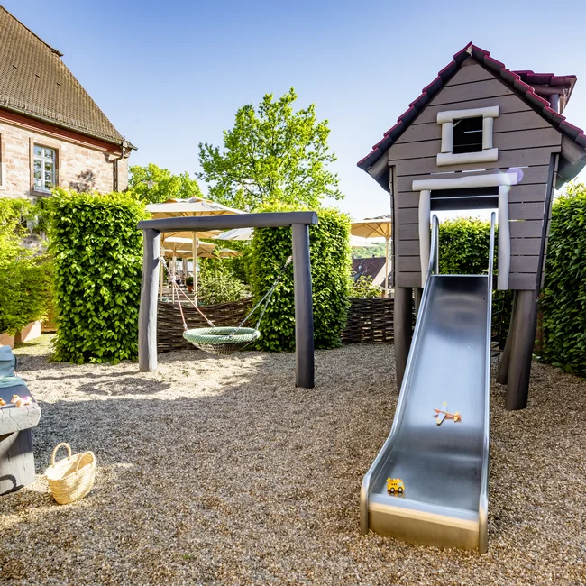 Inklusivleistungen im Kloster Hornbach und im Lösch Spielplatz mit Rutsche, Schaukel und Sitzbank neben Haus und grünen Hecken