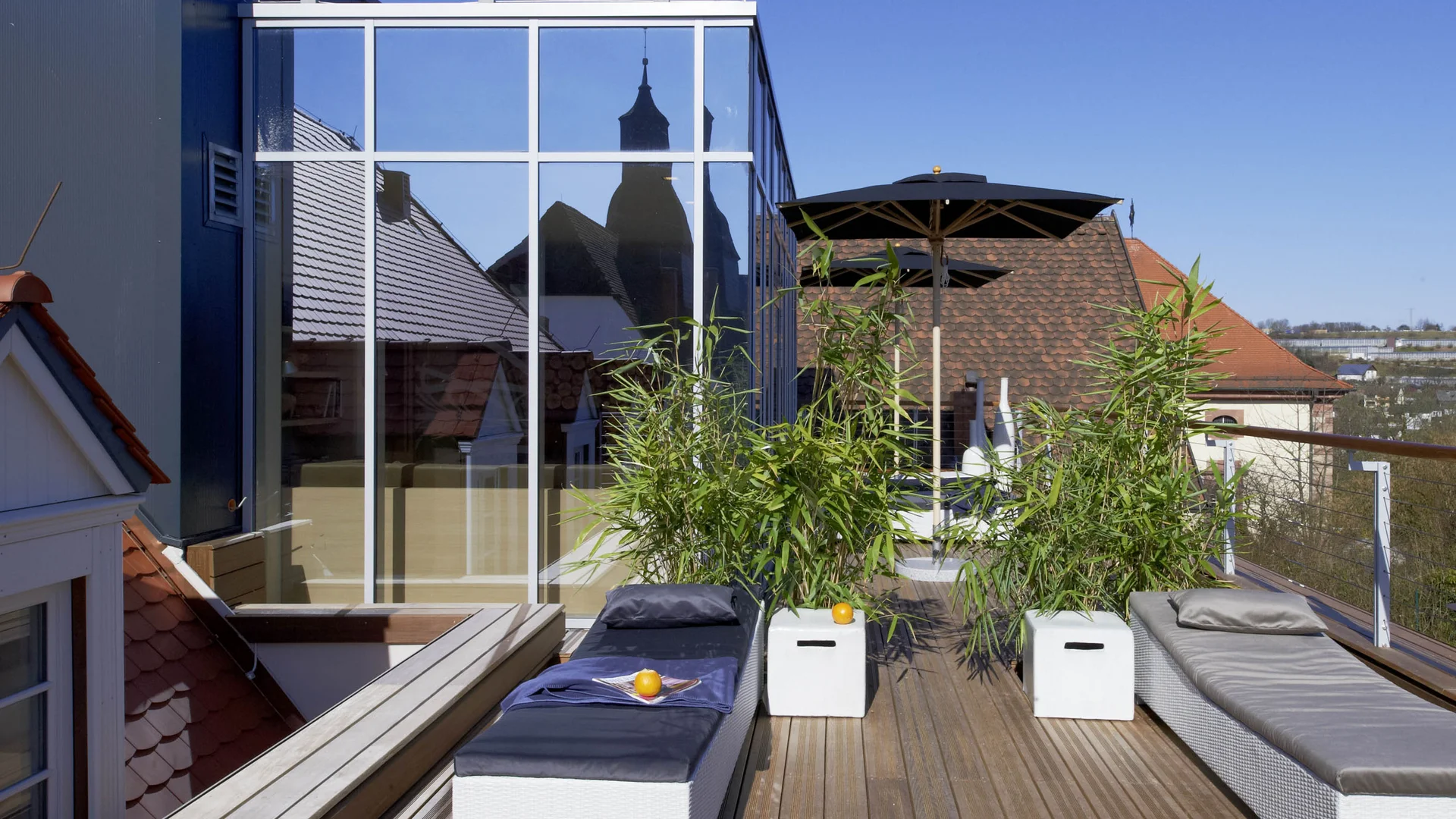 Escape to a countryside hotel with wellness facilities Rooftop terrace with loungers, plants, and church tower reflected in window