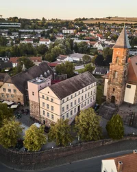 Kloster Hornbach: Ihre Ansprechperson für Medienanfragen Luftaufnahme einer kleinen Stadt mit Kirche, alten Gebäuden und grünen Bäumen
