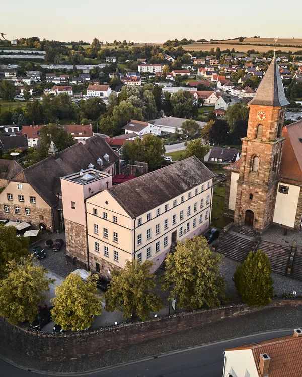 Ihr Urlaub im Klosterhotel an der Deutschen Weinstraße Luftaufnahme einer kleinen Stadt mit Kirche, alten Gebäuden und grünen Bäumen