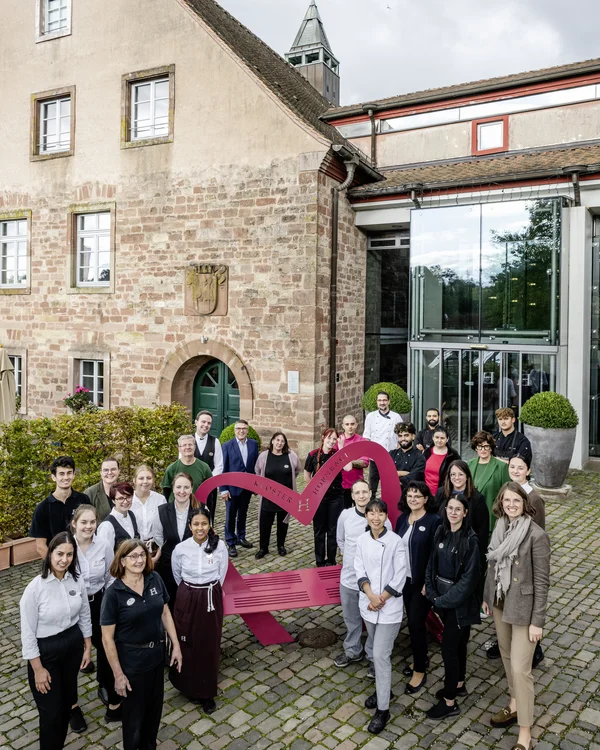 Ihre Gastgeber im Kloster Hornbach Gruppenfoto vor historischem Gebäude mit rot lackierter Bank in Herzform
