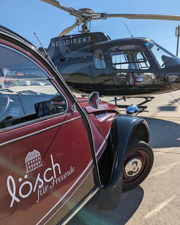 Exzellenter Lernort Kloster Hornbach Rotes Auto mit Lösch Werbung neben schwarzem Helikopter Helidirekt auf Flughafen