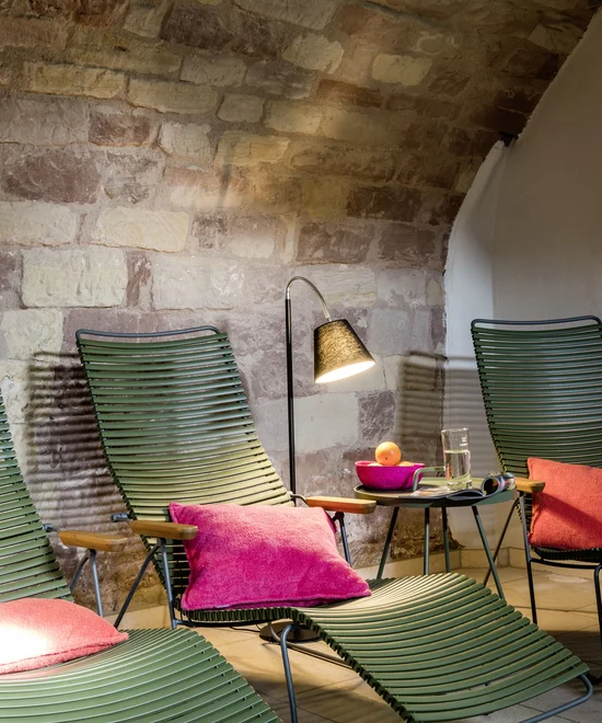 Suite AufEwig Grüne Liegestühle mit pinken Kissen und Lampe vor einer Steinwand