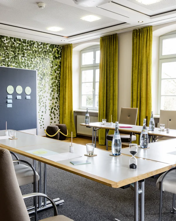 Exzellenter Lernort Kloster Hornbach Konferenzraum mit grünen Vorhängen, Tischen, Stühlen und Flipchartwand