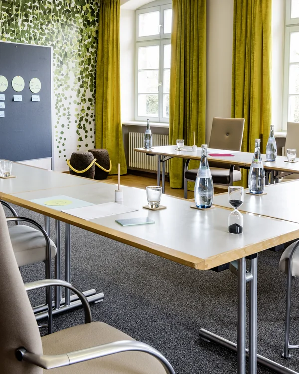 Ihr Tagungshotel Pfalz | Kreative Meetings im historischen Kloster Hornbach Konferenzraum mit grünen Vorhängen, Tischen, Stühlen und Flipchartwand