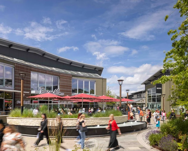 Ausflugstipps für Ihren Urlaub in der Pfalz Belebter Einkaufsbereich mit Café und roten Sonnenschirmen unter blauem Himmel