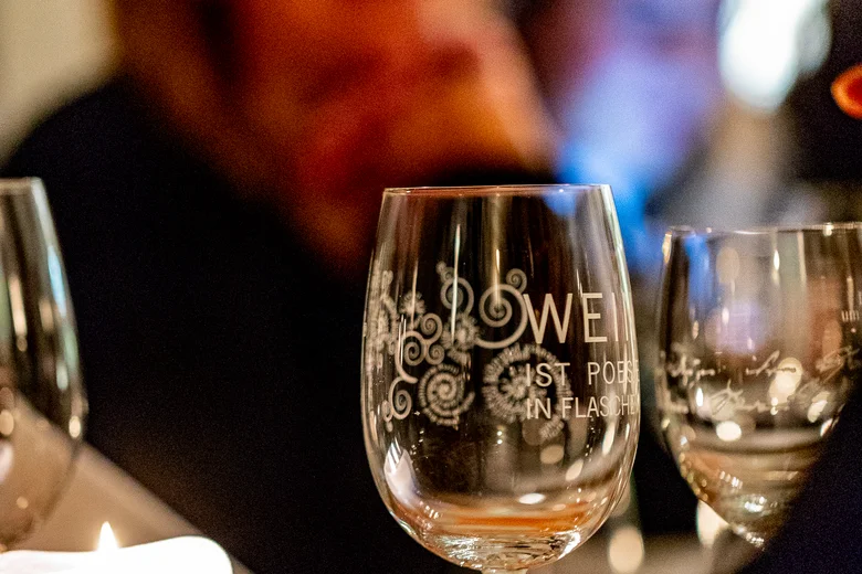 Pfälzer Wein. Pfälzer Land. Pfälzer Lebensart. Gläser und Kerze auf einem Tisch bei einem Abendessen mit unscharfen Personen im Hintergrund