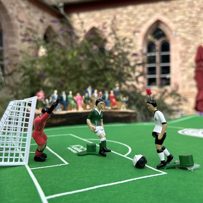 Exzellenter Lernort Kloster Hornbach Tischfußballspieler auf grünem Spielfeld vor einem Tor mit Zuschauern im Hintergrund