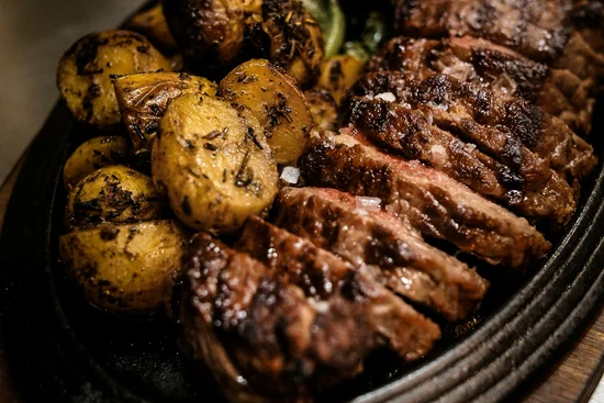 ABBA-Dinner – A Night to Remember Gegrilltes Steak mit Bratkartoffeln und grünen Paprikaschoten auf einer gusseisernen Platte