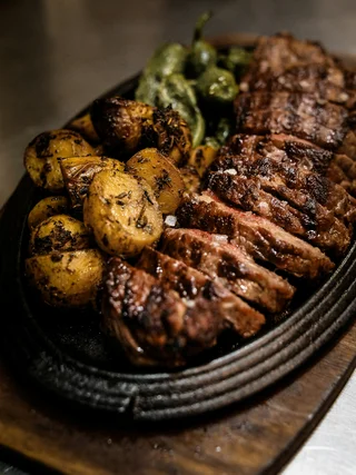 Treffpunkt, Kraftplatz und Hotel in Hornbach Gegrilltes Steak mit Bratkartoffeln und grünen Paprikaschoten auf einer gusseisernen Platte