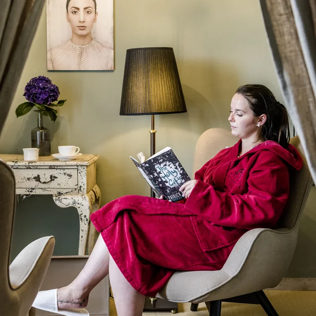 Inklusivleistungen im Kloster Hornbach und im Lösch Frau in rotem Bademantel liest in einem Sessel in gemütlichem Zimmer