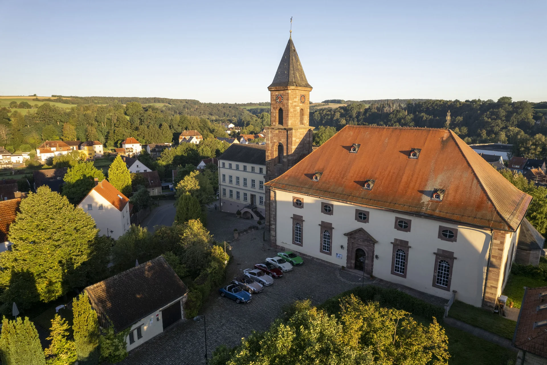 Exzellenter Lernort Kloster Hornbach Historische Kirche mit rotem Dach und Turm in einem grünen Dorf in der Abendsonne