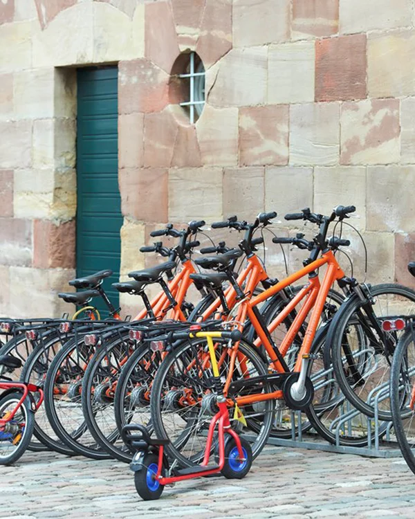 Kloster Hornbach: Ihr fahrradfreundliches Hotel in der Pfalz Mehrere orange Fahrräder und ein roter Scooter vor einer Steinmauer geparkt