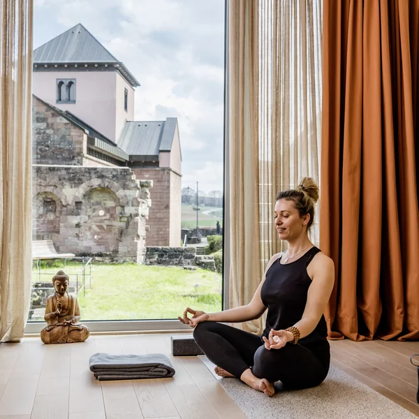 Escape to a countryside hotel with wellness facilities Woman meditating on yoga mat by large window with view of historic buildings