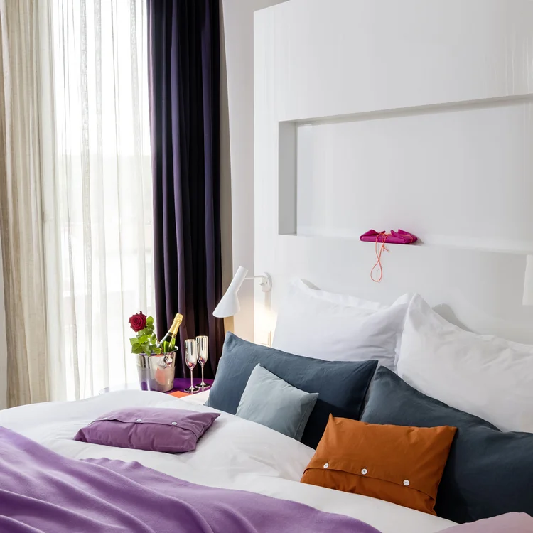 Treffpunkt, Kraftplatz und Hotel in Hornbach Helles Hotelzimmer mit Bett, lila Decke, bunten Kissen und Champagner mit Rose