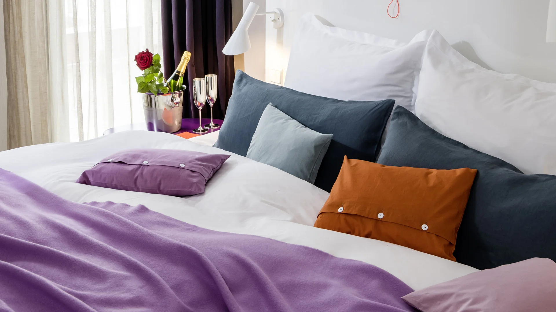 Treffpunkt, Kraftplatz und Hotel in Hornbach Helles Hotelzimmer mit Bett, lila Decke, bunten Kissen und Champagner mit Rose