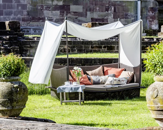 Treffpunkt, Kraftplatz und Hotel in Hornbach Gemütliche Sitzbank mit Kissen und Sonnenschutz im Garten vor Steinmauer