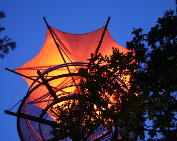 Ausflugstipps für Ihren Urlaub in der Pfalz Beleuchteter Aussichtsturm mit oranger Segelstruktur bei Abenddämmerung