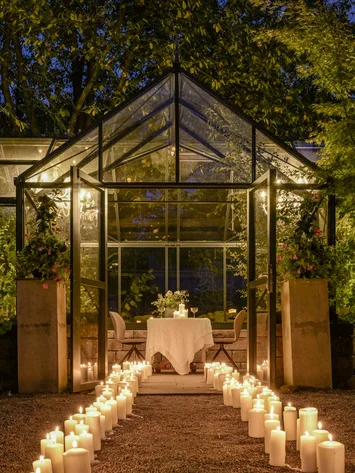 Our venue, your dream wedding Glass greenhouse decorated with candles leading to a candlelit dinner table