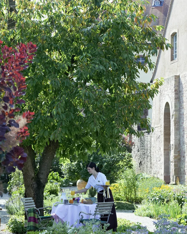 Brunch und Frühstück im Kloster bei Zweibrücken Kellnerin deckt Tisch im Garten neben altem Gebäude an sonnigem Tag