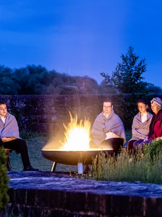 Treffpunkt, Kraftplatz und Hotel in Hornbach Menschen sitzen abends um ein offenes Feuer im Freien, eingehüllt in Decken