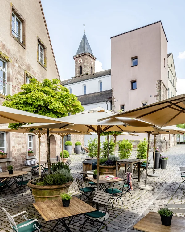 Von gemütlich bis Gourmet: Restaurants im Kloster Hornbach Sonnige Außenterrasse eines Cafés mit Tischen, Stühlen und sonnenschirmen