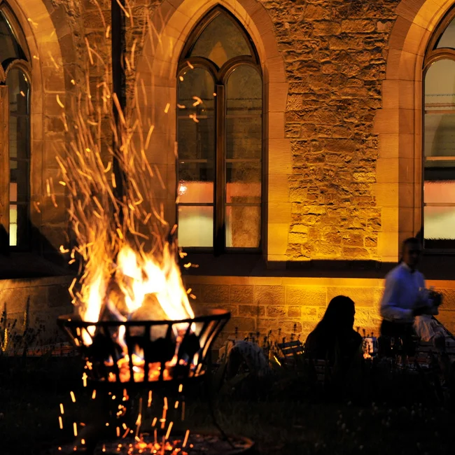 Inklusivleistungen im Kloster Hornbach und im Lösch Menschen sitzen bei Feuerkorb vor beleuchtetem steinernen Gebäude bei Nacht