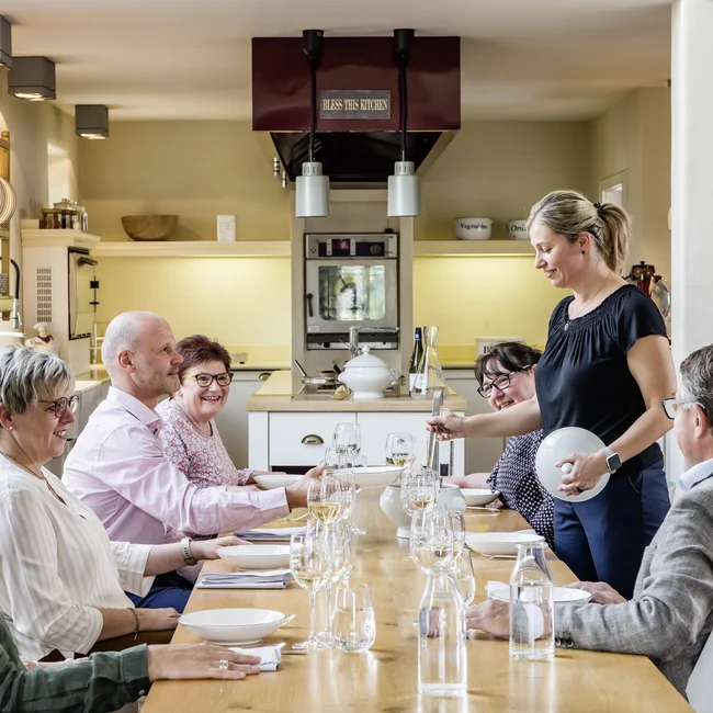 Wollen Sie das gesamte Landhaus mieten? Gruppe älterer Personen am Esstisch in heller Küche, Frau serviert Essen