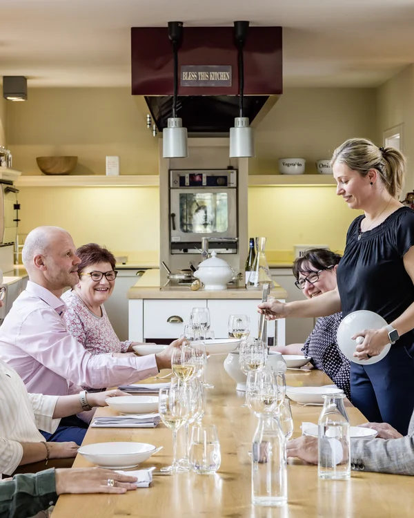 Kulinarik im Lösch: Gaumenfreuden der besonderen Art Gruppe älterer Personen am Esstisch in heller Küche, Frau serviert Essen