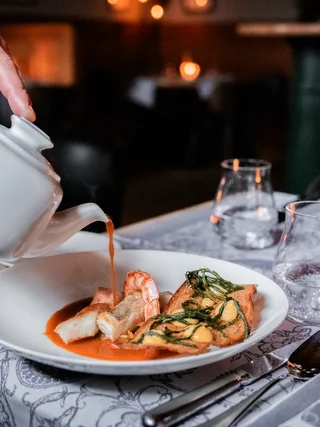 Treffpunkt, Kraftplatz und Hotel in Hornbach Hand gießt Sauce aus Kanne über Gourmetgericht in weißem Teller im Restaurant