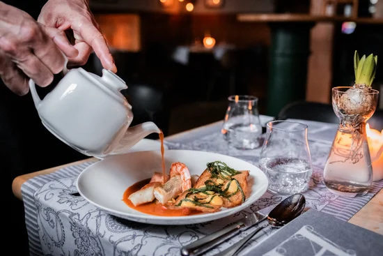 ABBA-Dinner – A Night to Remember Hand gießt Sauce aus Kanne über Gourmetgericht in weißem Teller im Restaurant