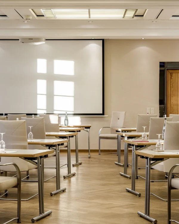Tagungsräume Pfalz | Historische & moderne Räume im Kloster Hornbach Heller Konferenzraum mit weißen Stühlen, Tischen und Projektionsleinwand