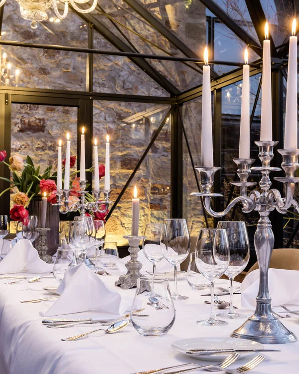 Our venue, your dream wedding Elegant table with candelabras, candles, glasses, and flowers in a glass greenhouse