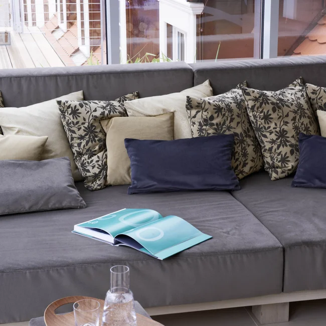 Escape to a countryside hotel with wellness facilities Gray sofa with patterned pillows in front of large window showing roof tiles