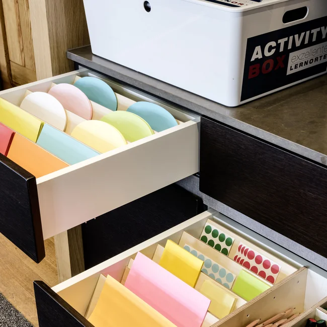 Exzellenter Lernort Kloster Hornbach Offene Schubladen mit buntem Papier und Stiften neben einer weißen Activity Box