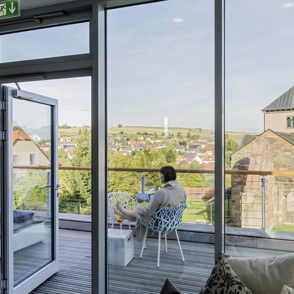 Escape to a countryside hotel with wellness facilities Person sitting with laptop on balcony overlooking village and church