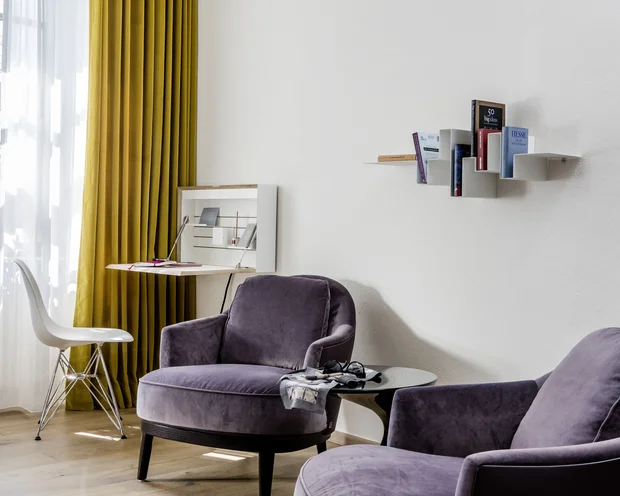 Treffpunkt, Kraftplatz und Hotel in Hornbach Gemütliche Sitzecke mit lilafarbenen Sesseln und Bücherregal an weißer Wand